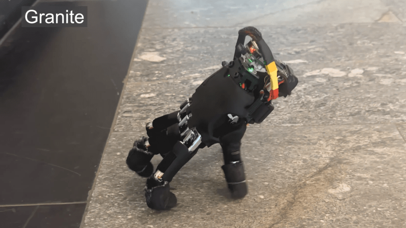 A black robotic hand is shown walking across a granite floor, using its fingers as legs.