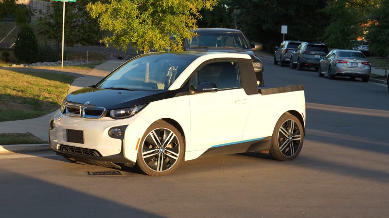 A two door pickup or ute in white with a black hood and blue accents. It's built from a chopped up BMW i3 REX EV.